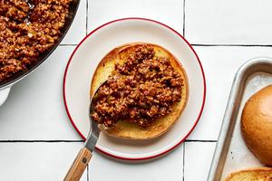 sloppy joe ground beef being spooned on to a buttered toasted hamburger bun