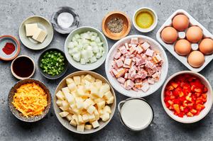 bacon, potatoes, onion, bell pepper, heavy cream, paprika, seasoning, cheddar, butter and eggs in bowls for breakfast hash