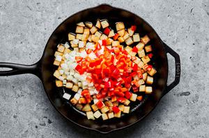 onions, potatoes, and bell peppers being cooked in a skillet with bacon grease