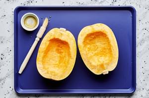 a spaghetti squash halved, with seeds removed and being brush with olive oil on a baking sheet
