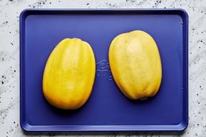 a spaghetti squash that has been halved, seeds removed and brushed with olive oil face down on a baking sheet ready to roast