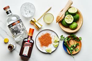 limes, serrano pepper, tequila, tripe sec, cilantro, angostura bitters and Tajín on the counter to make a spicy margarita