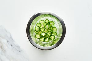 sliced serrano pepper being muddled with lime juice in a cocktail shaker for a spicy margarita