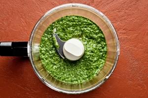 Spinach pesto in a food processor made with spinach, basil, Parmesan, garlic, pine nuts, and salt.