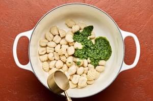 spinach pesto and reserved pasta water liquid being added to a pot with cooked gnocchi