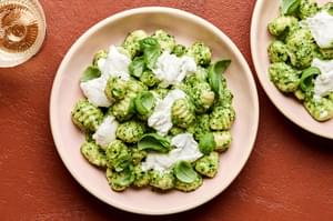 a bowl of spinach pesto gnocchi topped with creamy burrata and garnished with fresh basil