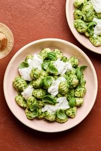 a bowl of spinach pesto gnocchi topped with creamy burrata and garnished with fresh basil
