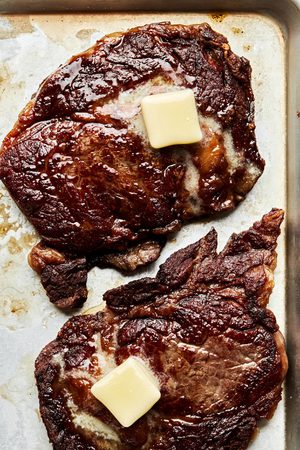 cooked ribeye steaks resting on a baking sheet topped with butter