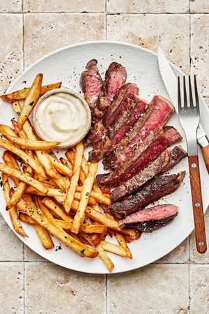 Homemade steak frites with juicy ribeye steak sliced and served alongside crispy golden fries and garlic aioli dipping sauce