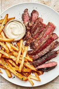 Homemade steak frites with juicy ribeye steak sliced and served alongside crispy golden fries and garlic aioli dipping sauce