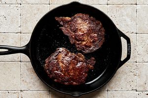 ribeye steaks seasoned with salt being cooked in olive oil in a skillet to serve with homemade steak frites
