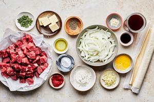 stew beef, onion, beef broth, flour, tomato paste thyme, spices and puff pastry on the counter to make steak pie