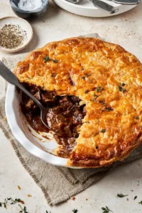 A homemade steak pie on the counter with a slice cut out made with stew beef, onion,  tomato paste, spices and Worcestershire