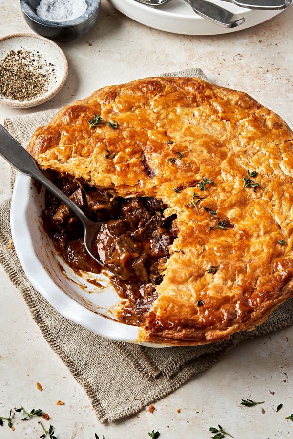 A homemade steak pie on the counter with a slice cut out made with stew beef, onion, tomato paste, spices and Worcestershire