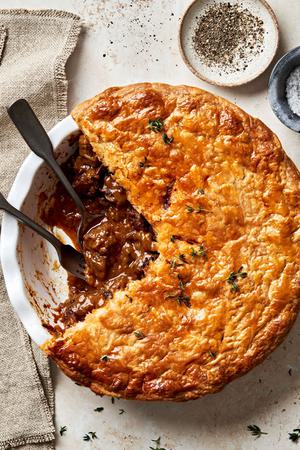 A homemade steak pie on the counter with a slice cut out made with steak, onion, tomato paste, spices and Worcestershire