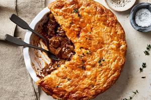 A homemade steak pie on the counter with a slice cut out made with stew beef, onion, tomato paste, spices and Worcestershire