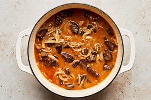 steak pie filling being simmered in a dutch oven made with onions, tomato paste, beef stock, thyme and other spices
