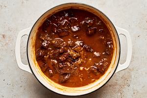 steak pie filling being simmered in a dutch oven made with onions, tomato paste, beef stock, thyme and other spices