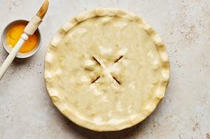 steak pie topped with puff pastry that has been crimped on the edges and the top has been brushed with melted butter
