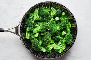 broccoli being steamed in a pot of salted water with a steamer basket set inside