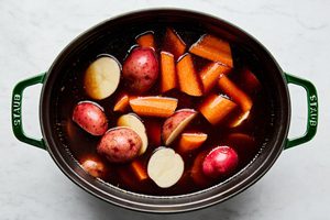 potatoes and carrots simmering in a dutch oven in corned beef reserved liquid while the beef rests