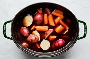 potatoes and carrots simmering in a dutch oven in corned beef reserved liquid while the beef rests
