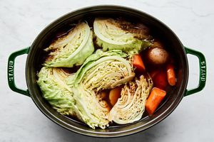 cabbage added to a pot with potatoes and carrots cooking in corned beef liquid