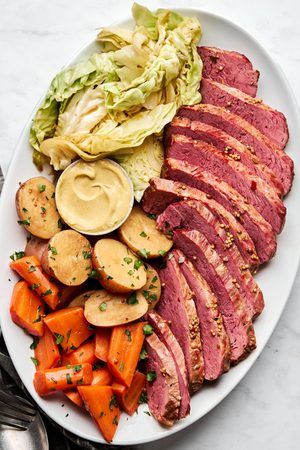 sliced Corned beef and cabbage, with potatoes, carrots and mustard on a large serving platter, an Irish comfort food meal