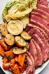 sliced Corned beef and cabbage, with potatoes, carrots and mustard on a large serving platter, an Irish comfort food meal