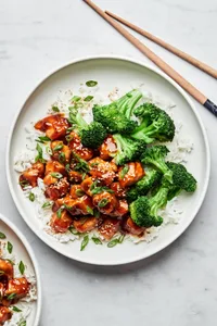 homemade teriyaki chicken on a plate served over white rice with steamed broccoli on the side next to chop sticks
