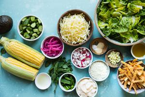 romaine, corn, cheese, radishes, pickled onion, avocado, tortilla strips, cucumber, oil, jalapeño,  and spices in bowls