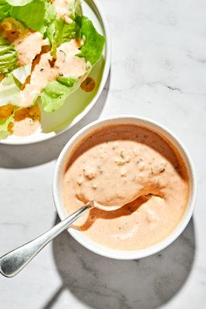 a bowl of homemade thousand island dressing being spooned over a green salad