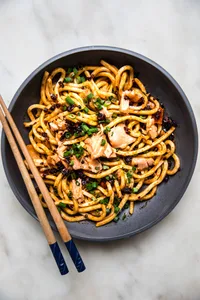 Bowl filled with udon noodles topped with green onions, smoked salmon and chili crisp