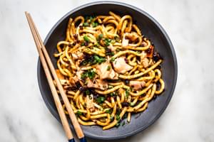 Large bowl filled with udon noodles, smoked salmon and chili crisp topped with green onions