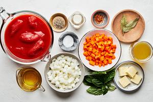 butter, carrots, onion, tomatoes, olive oil, bay leaves, salt, pepper, chicken stock, cream and basil in bowls for bisque