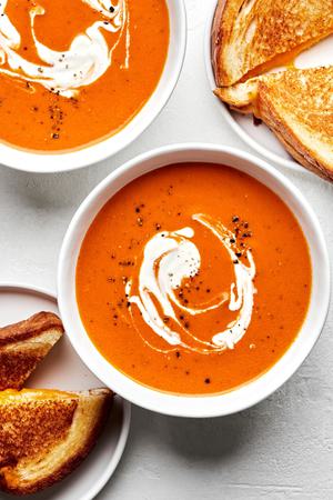 2 bowls of homemade tomato Soup topped with a swirl served with grilled cheese sandwiches