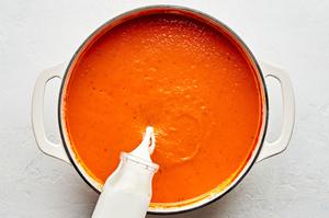cream being poured into a pot of homemade tomato Soup made with carrots, onion, tomatoes, basil and cream