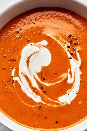 a bowl of homemade tomato Soup topped with a swirl of cream made with carrots, onion, tomatoes, basil and cream