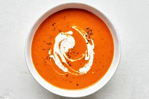 a bowl of homemade tomato Soup topped with a swirl of cream made with carrots, onion, tomatoes, basil and cream