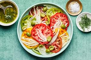 tomatoes and fennel on a platter surrounded by salad dressing, flaky salt and fresh dill