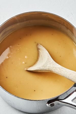 a pot of homemade turkey gravy seasoned with thyme, bay leaf and parsley being stirred with a wooden spoon