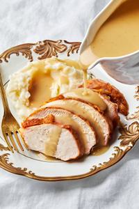 homemade turkey gravy seasoned with thyme, bay leaf and parsley being poured over turkey and mashed potatoes