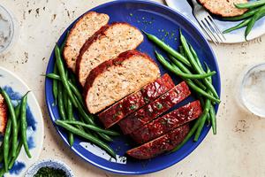 homemade turkey meatloaf with a brown sugar sauce sliced on a serving plate surrounded by bright green beans