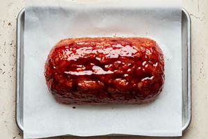 Turkey meatloaf on a parchment lined baking sheet coated with a brown sugar sauce ready to be baked in the oven