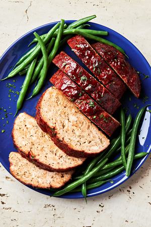 homemade turkey meatloaf with a brown sugar sauce sliced on a serving plate surrounded by bright green beans