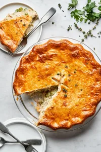 a homemade turkey pot pie filled with turkey, celery, carrot, onion & peas with a slice cut out sitting on plate next to it