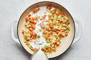 milk being added to a skillet with cooked celery, onion, carrots, flour and spices making the filling for turkey pot pie