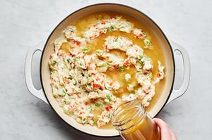 turkey stock being added to a skillet with milk, vegetables, flour and spices making the filling for turkey pot pie