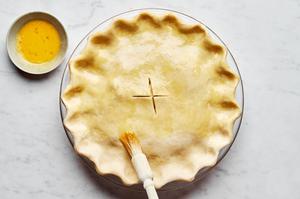 an unbaked turkey pot pie being brushed with egg wash ready to be baked in the oven
