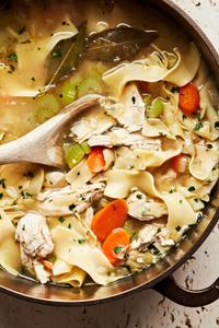 a pot of homemade turkey soup being stirred with a wooden spoon made with carrots, celery, onions and noodles